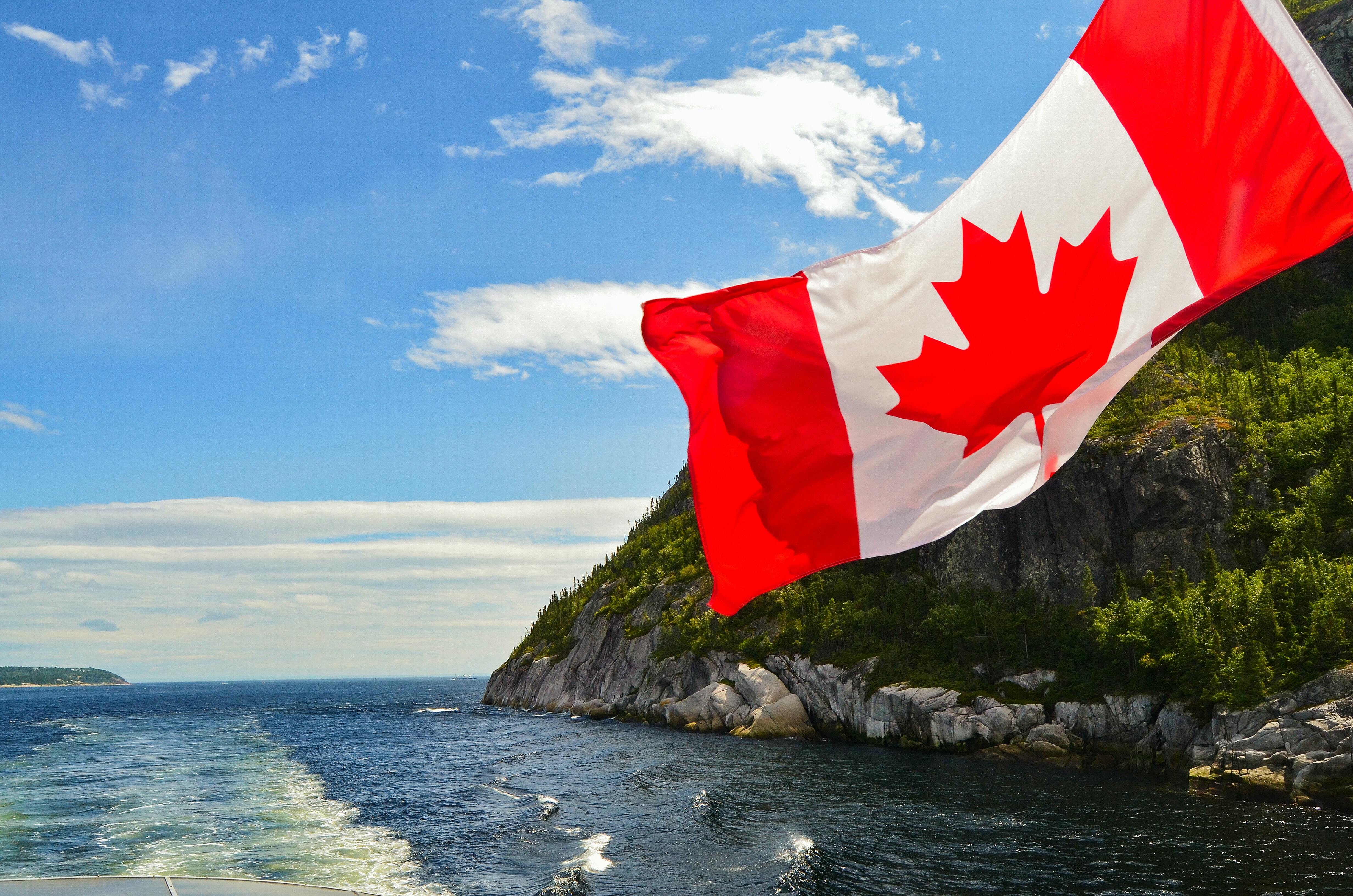 Canadian flag with cliffs and ocean background on a sunnet day.